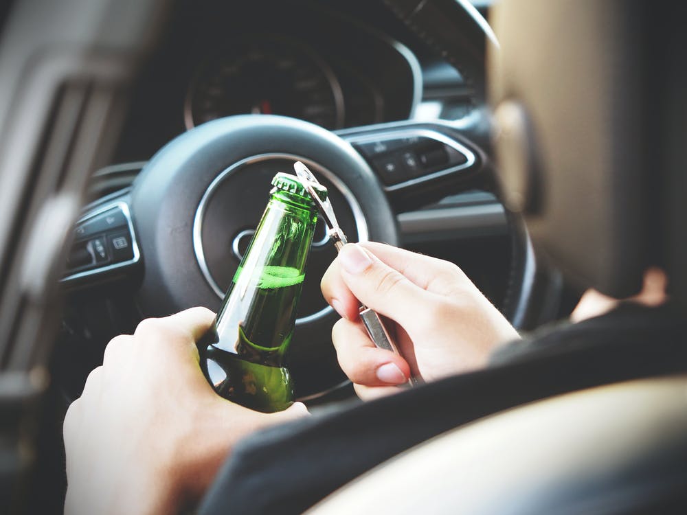 Driver of a car sitting in the driver's seat while opening a beer bottle with a beer bottle opener. An investigation for Driving Under the Influence, also known as DUI or DWI, might begin soon.